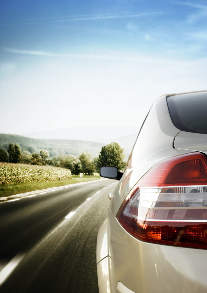 back side of a car on a road with mountains and trees in front of it